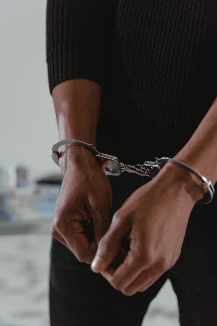 Close-up of an adult's hands in handcuffs wearing a black sweater indoors.